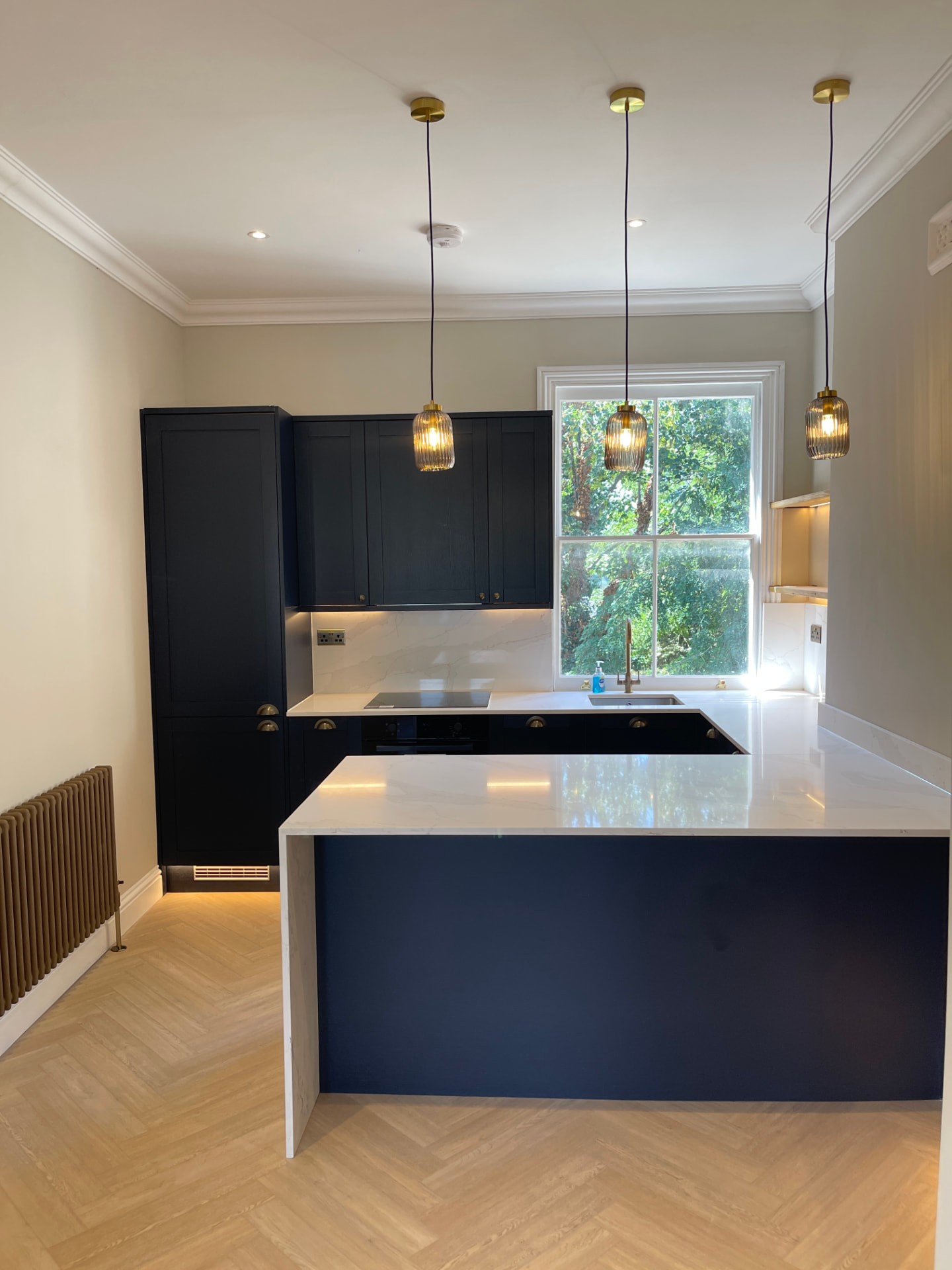 Clean galley kitchen with brass pendant lights and parquet floor